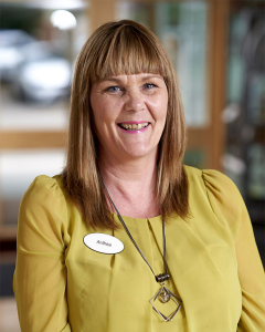 Image of the female care home manager for Robert Harvey House, wearing a lemon coloured top, smiling and with shoulder length hair cut with a fringe.